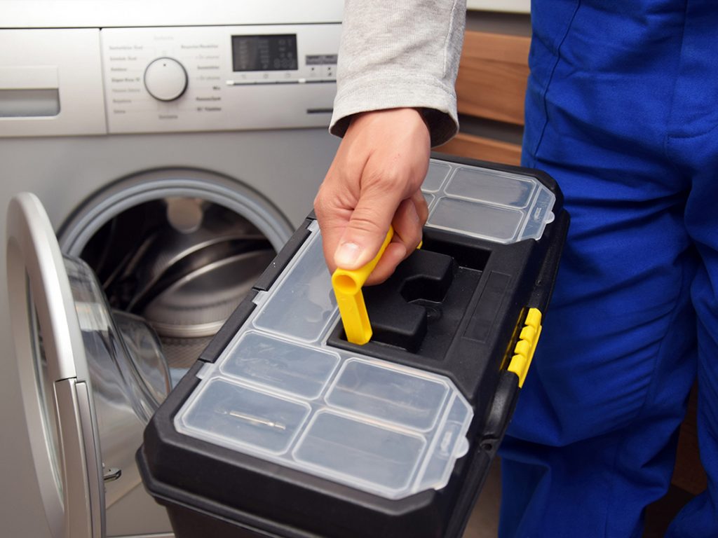 Reparación de lavadoras Indesit Fotografía de técnico sujetando una caja de herramientas delante de una lavadora.